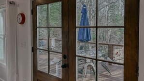 Una puerta de madera con un panel de vidrio, un reloj rojo y vista a una terraza exterior con sillas y un paraguas.