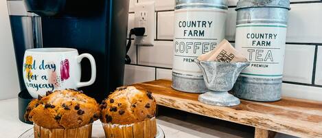 Una encimera de cocina con una cafetera, dos muffins y dos recipientes metálicos etiquetados como 'Country Farm Coffee' y 'Country Farm Tea'.