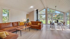 Ein geräumiges Wohnzimmer mit einer großen Couch, einem Couchtisch und einem Essbereich mit Tisch und Stühlen. Ein großes Fenster bietet Blick ins Freie.