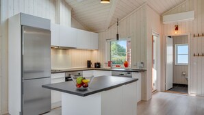 Eine moderne Küche mit einem Edelstahlkühlschrank, weißen Schränken, einer zentralen Kochinsel mit Obst und einem Fenster, das für natürliches Licht sorgt.