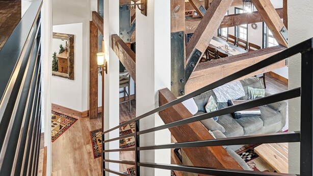 A staircase with wooden beams and metal railings, leading to a dining area with a high ceiling and exposed beams.