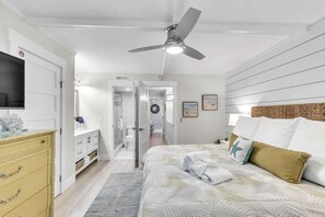 A bedroom with a bed, a ceiling fan, a TV, and a bathroom visible through an open door.