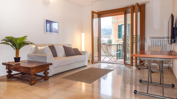 Una sala de estar moderna con sofá, una mesa de centro de madera, una planta en maceta y vistas a un balcón con una silla.