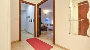 Un pasillo con alfombra roja, puertas de madera y un área de estar con sofá y lámpara.