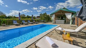 Una piscina con sillones de playa y sombrillas, un jacuzzi y una zona de estar cubierta.