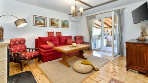Una sala de estar acogedora con un sofá rojo, una mesa de centro de madera y una araña. Hay cuadros en la pared, un televisor y un mueble de madera.