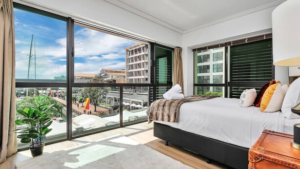 Une chambre moderne avec un grand lit, une vue sur la ville et une plante en pot.