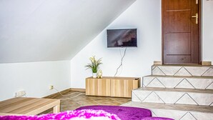 A modern living room with a sloped ceiling, a mounted TV, a wooden console, and a staircase with patterned tiles. - Awesome apartment in Gdansk with WiFi (Gdansk)