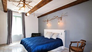 Un dormitorio con cama, una silla, techo de madera y lámpara con forma de rama.