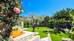 Un patio con un muro de piedra, un pequeño jardín y un sendero que conduce a un edificio.