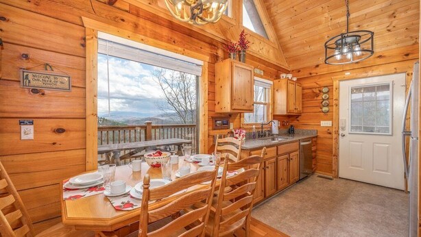 A wooden cabin with a dining area, kitchen, and a view of the outdoors.