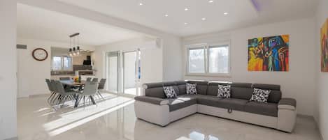 A spacious living area with a large sectional sofa, a dining table with chairs, and a kitchen in the background.