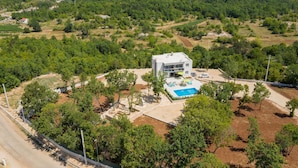 Una moderna casa a due piani con piscina, immersa tra alberi e un paesaggio collinare.