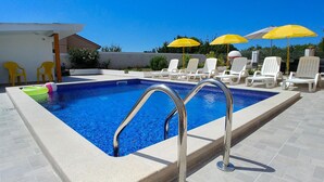Une piscine rectangulaire avec un escalier en métal, entourée de chaises longues blanches et de parasols jaunes.