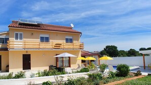 Un bâtiment à deux étages avec une façade jaune, un balcon doté de balustrades en bois et un espace piscine agrémenté de parasols jaunes.