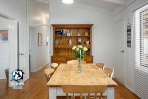 A dining area with a wooden table and chairs, a bookshelf, and a vase with flowers.