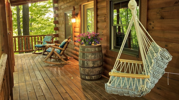 A wooden cabin with a porch, rocking chairs, a hanging chair, and a barrel with flowers. - Beechwood Cabin near Ash Cave (New Plymouth)