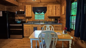 A wooden cabin kitchen with a dining table, chairs, a refrigerator, an oven, a microwave, and a window with curtains. - Beechwood Cabin near Ash Cave (New Plymouth)