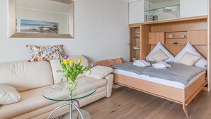 Un dormitorio moderno con cama, una mesita de vidrio, sofá y espejo.