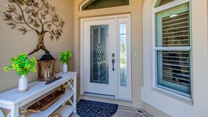 A front door with a glass panel, a metal tree decoration, a lantern, and a doormat. - Beautiful Water/Golfview 3 BR pool home,  located in the center of the Villages (The Villages)
