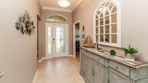 A hallway with a light fixture, a decorative wall piece, a door with glass panels, a cabinet with a plant, and a window with a view. - Beautiful Water/Golfview 3 BR pool home,  located in the center of the Villages (The Villages)