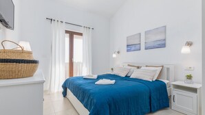 A bedroom with a large bed, white walls, a window with curtains, a bedside table with a lamp, and a wall-mounted shelf with a plant. - Awesome home in Betiga (Betiga)