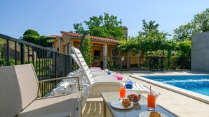 Ein Poolbereich mit Liegestühlen, einem Tisch mit Frühstücksangeboten und freiem Blick auf den Pool und die umliegenden Gebäude.