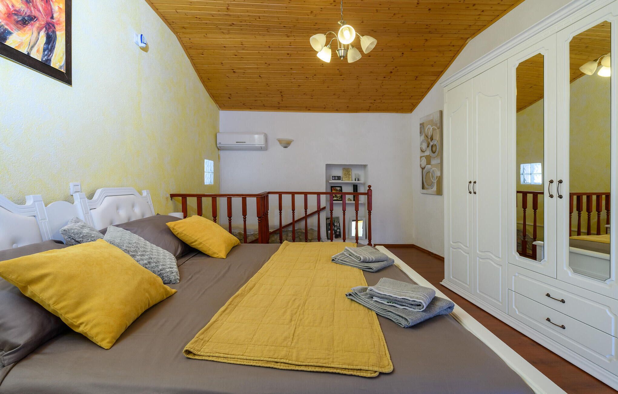 A bedroom with a bed, a wooden ceiling, a white wardrobe, and a staircase.