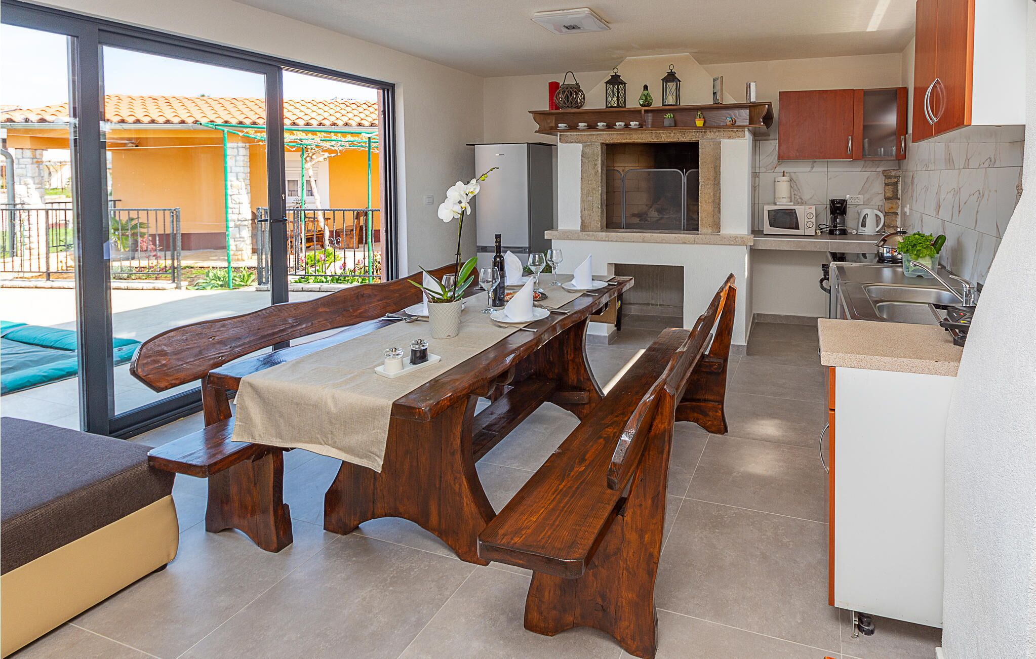 A modern kitchen with a dining area, featuring a wooden bench and table, a built-in oven, and a view of the outdoor patio.