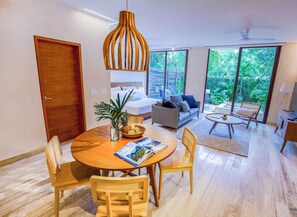 Un salon moderne comprenant un coin repas, un ensemble de canapés et une grande fenêtre donnant sur un paysage verdoyant.