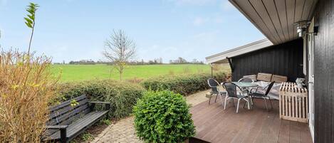 Eine Terrasse mit Tisch, Stühlen, einer Bank und einem Blumentopf.