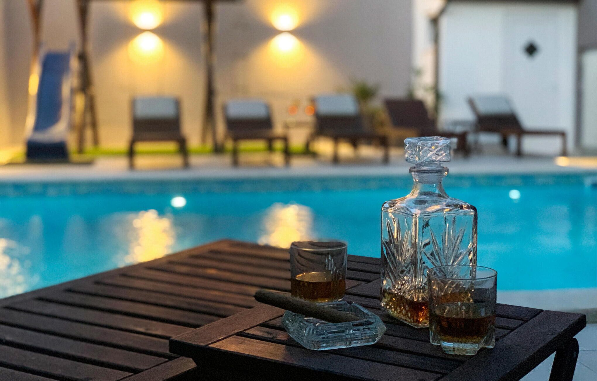 A poolside table with a bottle and glasses, a pool, and lounge chairs in the background.