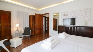 Habitació d'hotel amb un llit gran, una cadira, un escriptori amb una làmpada, un armari, una televisió i una paret amb un rètol decoratiu.