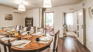 Una sala menjador amb una taula de fusta preparada per a sis persones, envoltada de cadires. Hi ha un bufet amb fruites i begudes, i un armari amb recipient de vidre.