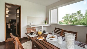 Zona de dinar amb taula de fusta, cadirees i preparació per esmorzar, incloent pa, suc i una cafetera.