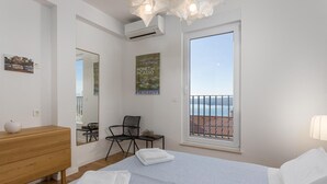 A bedroom with a bed, a wooden dresser, a chair, a small table, a mirror, and a poster. There is a large window with a view of the sea. - 3 bedroom gorgeous home in Crikvenica (Crikvenica)