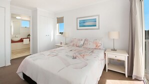 Une chambre d  ’hôtel comprenant un lit, des tables de chevet, un bureau, une fenêtre avec des rideaux, une salle de bain avec un lavabo et un miroir, et un tableau encadré au mur.