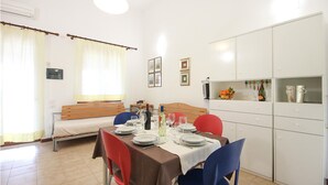 Een eetgedeelte met een tafel voor vier personen, een bank en een keuken met kasten en een wijnrek.