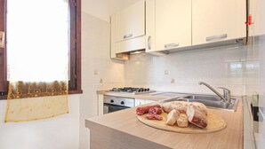 A kitchen with white cabinets, a gas stove, a sink, and a countertop with sliced bread and salami.