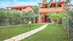 A pathway leading to a building with a tiled roof and a well-maintained lawn.