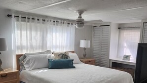 A hotel room with a bed, a ceiling fan, a nightstand, a lamp, a TV, and a window with curtains. - AQUAHOLIC VISTA (Englewood)