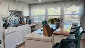 A modern kitchen with white cabinets, a tiled backsplash, and a central island with a wooden countertop. - AQUAHOLIC VISTA (Englewood)