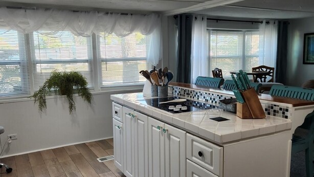 A modern kitchen with white cabinets, a central island, and a dining area with blue chairs. - AQUAHOLIC VISTA (Englewood)