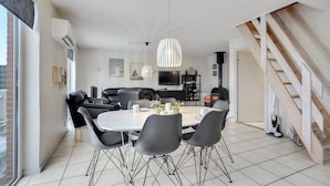 A modern living room with a dining area, featuring a fireplace, a TV, and a staircase.