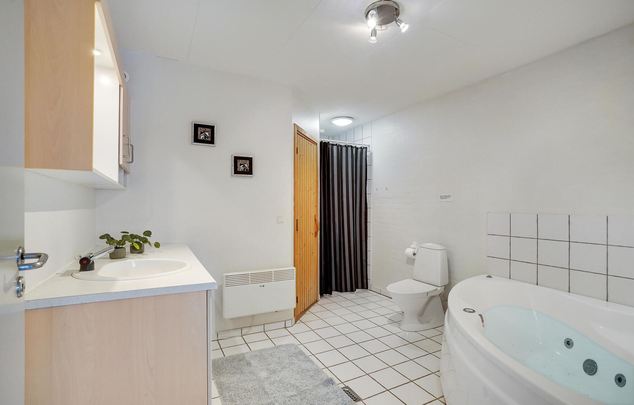 A modern bathroom with a white sink, toilet, and bathtub, wooden cabinets, and a shower curtain.
