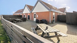 A building with a brick exterior, a sloped roof, and a wooden deck with picnic tables and chairs.