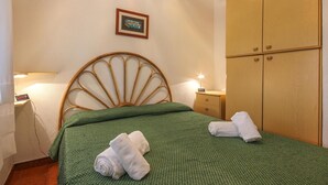 A neatly made bed with green bedding, a wooden headboard, and two rolled towels on the bed.