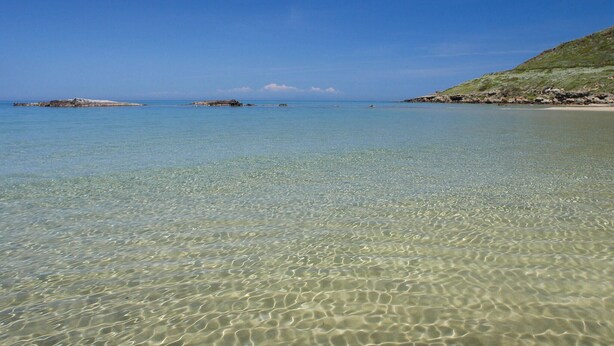 A clear, shallow coastal water body with rocky outcrops and a distant landmass.