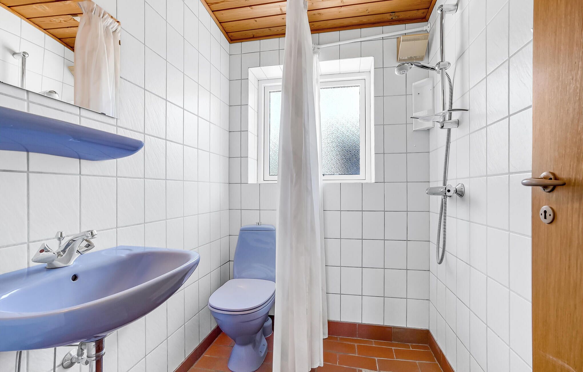 A bathroom with a sink, toilet, shower, and a window.