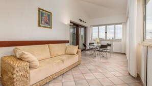 A spacious living area with a beige sofa, a dining table with chairs, and a large window offering a view.